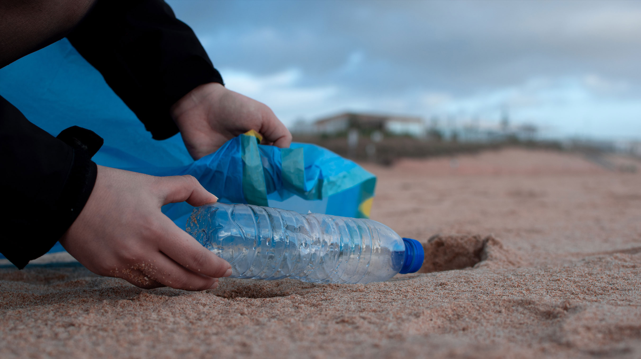 Someone picking up a plastic bottle from a beach